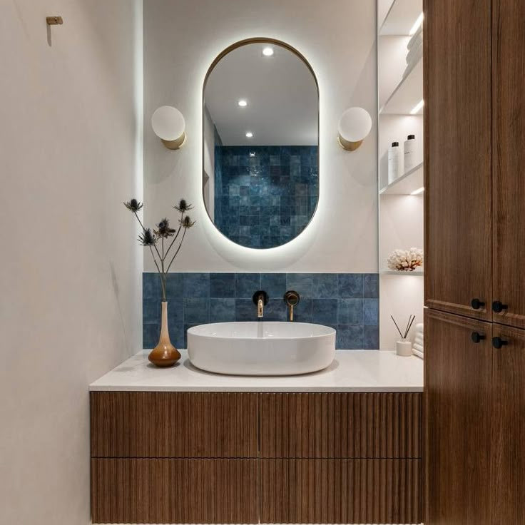 Modern bathroom with wooden vanity, white sink, and oval mirror.