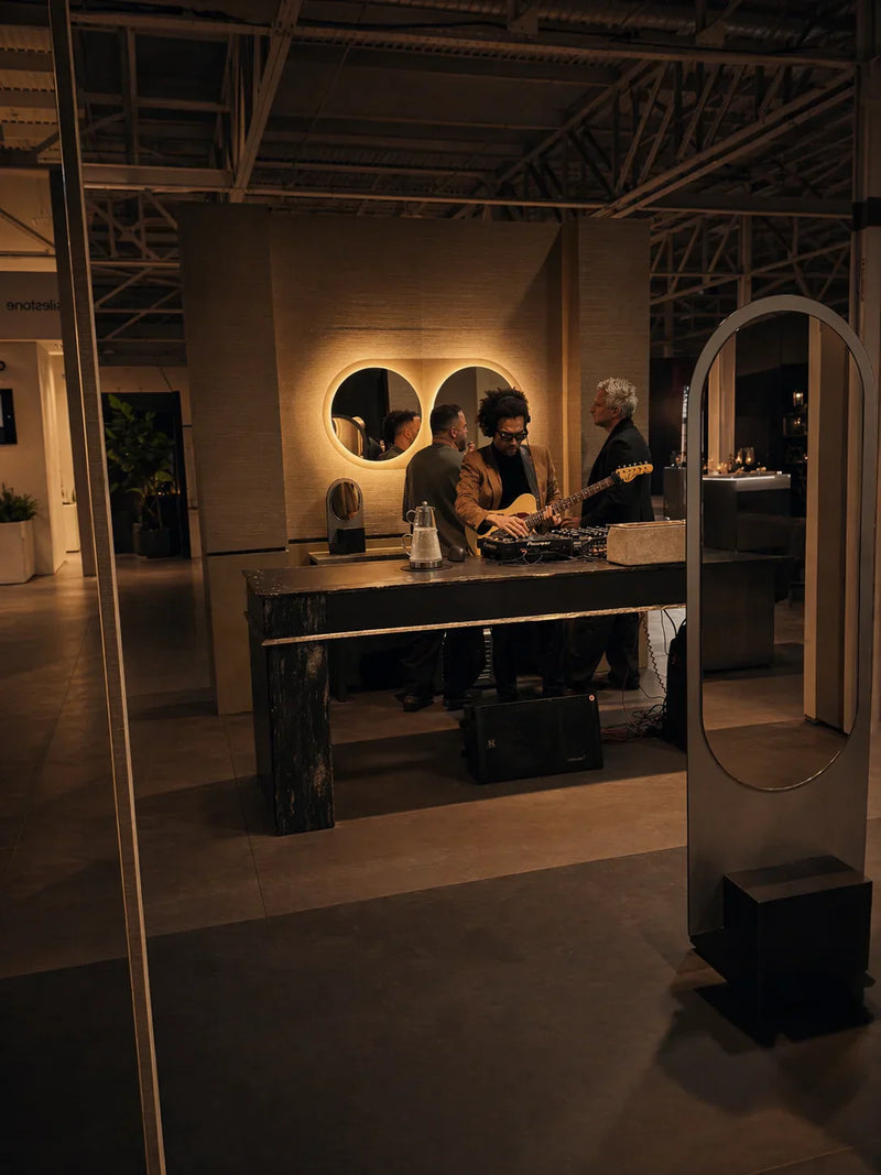 Evening reception at the Claris booth, Living Luxe 2025, Toronto Congress Centre. Twin Gemini backlit circle mirrors on a grasscloth wall, an Alice mirror floor sculpture visible to the right.
