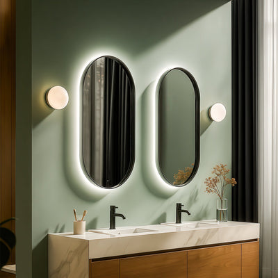 Bathroom vanity with two oval mirrors and light fixtures on a green wall.