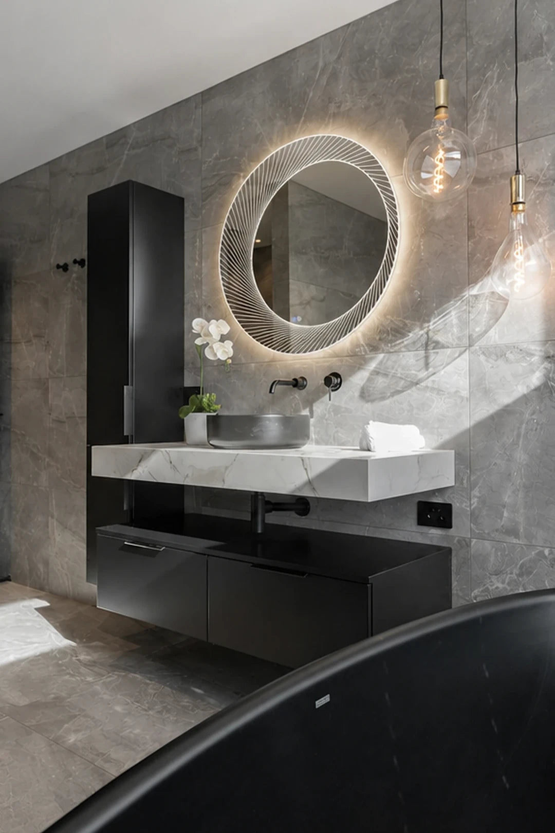 Claris ORSO mirror in a grey marble bath with a black floating vanity and pendant bulbs